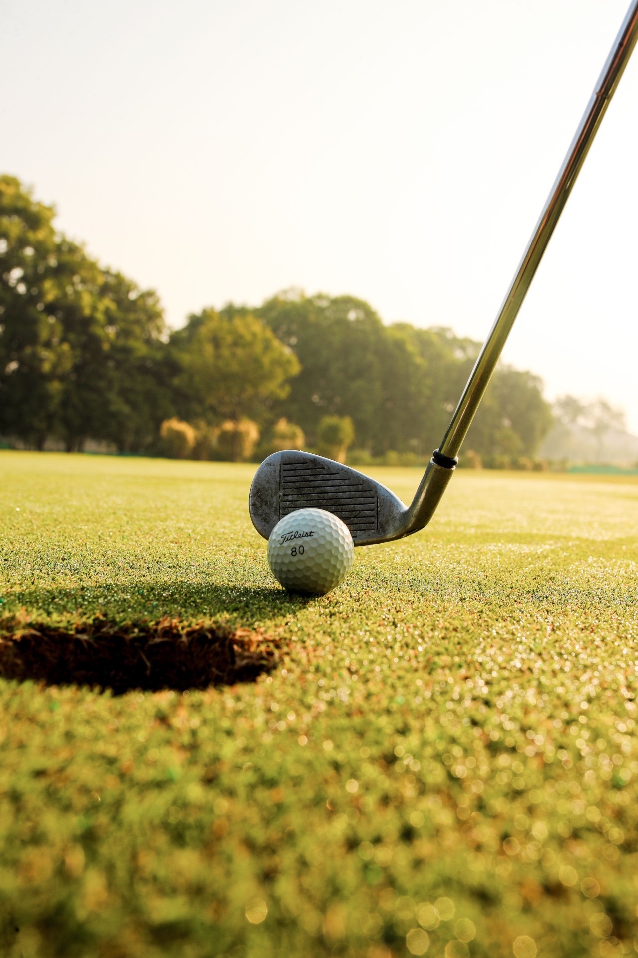 Iron addressing a golf ball on a dew-covered green at sunrise